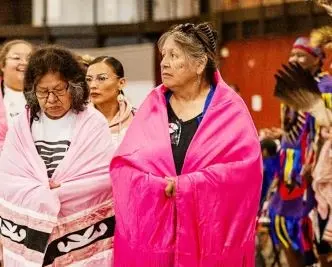 Native American women wearing pink shawls.