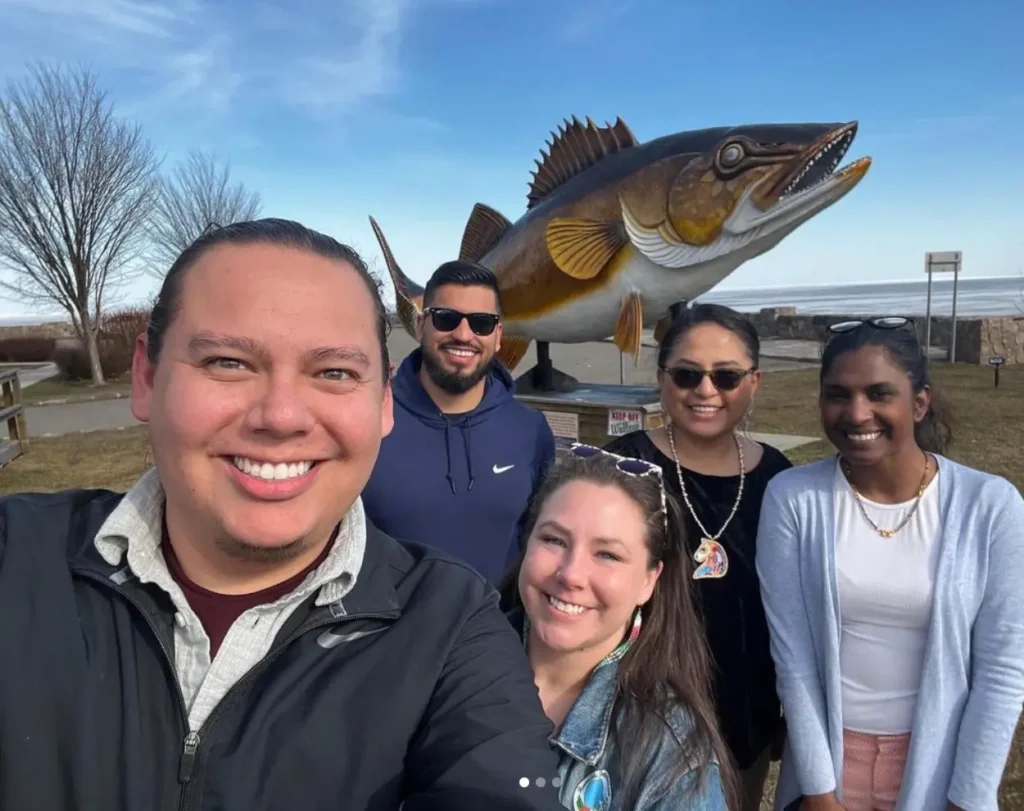 Five smiling people in front of a huge outdoor fish sculpture