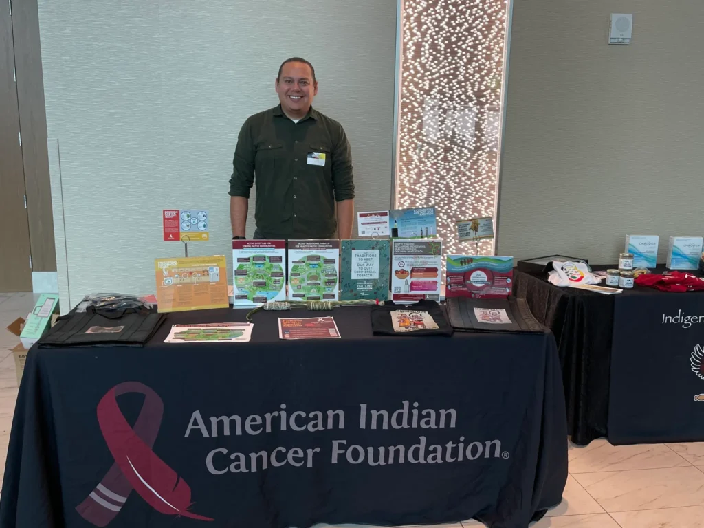 American Indian Cancer Foundation information table with booklets and publications and a staff member standing behind the table